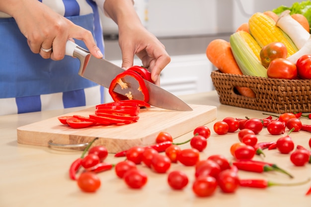 O cozinheiro no avental azul corta legumes. O conceito de produtos ecológicos para cozinhar