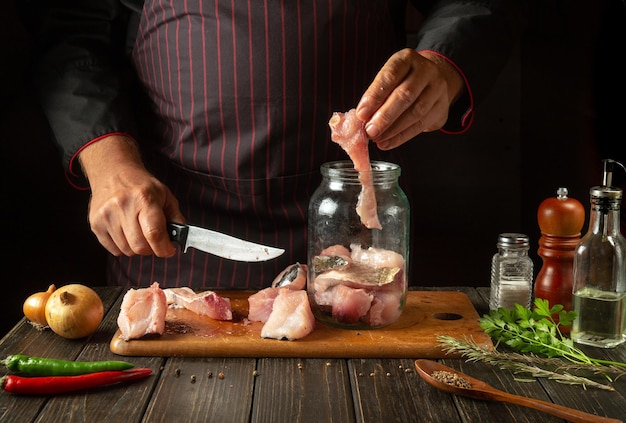 O cozinheiro prepara arenque na cozinha a partir de bifes de peixe e especiarias aromáticas, enlatando peixe em um frasco com sal e coentro.