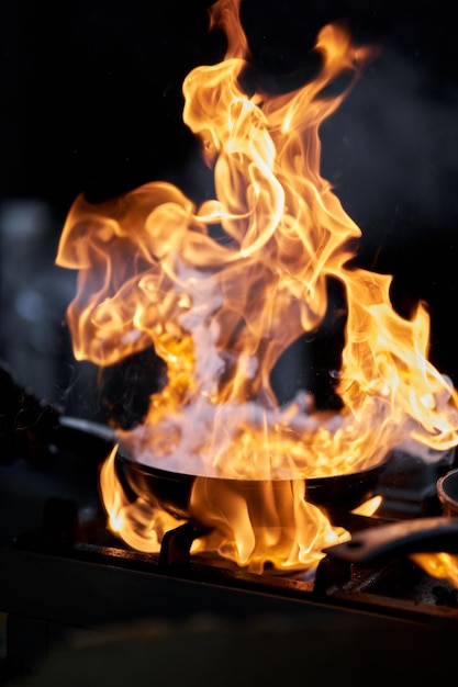 O cozinheiro prepara o molho em uma frigideira com chef de fogo cozinhando processamento de alimentos com chama