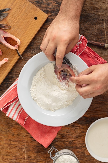 O cozinheiro prepara peixe fresco em uma mesa de madeira na cozinha de casa