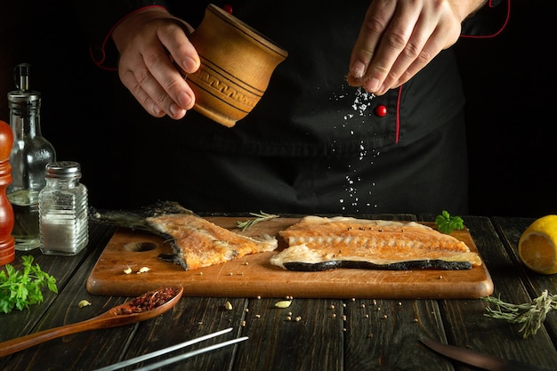 O cozinheiro prepara salmão fresco, peixe, truta, smorgus, espalhando os ingredientes com sal.