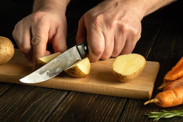 O cozinheiro prepara um prato de legumes na mesa da cozinha A faca para cortar legumes na mão do cozinheiro