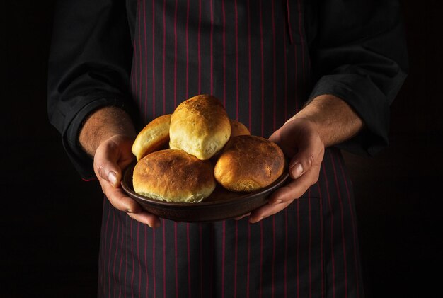 O cozinheiro segura em suas mãos um prato com tortas ou pães recém-assados Espaço preto livre para menu