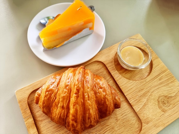 O croissant com leite condensado em uma placa de madeira e bolo de laranja em uma placa branca