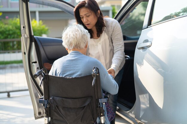 O cuidador ajuda e apoia a idosa asiática sentada na cadeira de rodas, prepare-se para chegar ao carro para viajar nas férias
