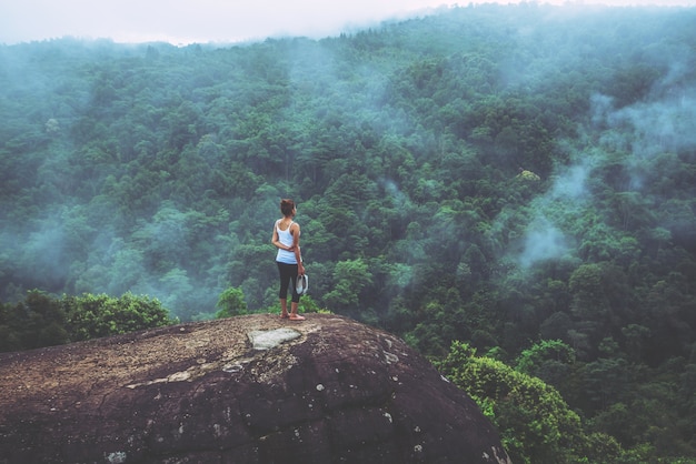 O curso asiático das mulheres relaxa no feriado. Mãos eretas em um penhasco rochoso. Madeira natureza selvagem no m