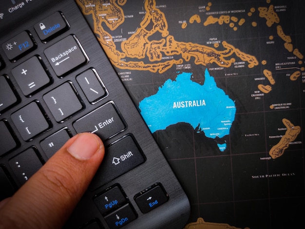 O dedo está pressionando enter no teclado preto que está acima do mapa da austrália