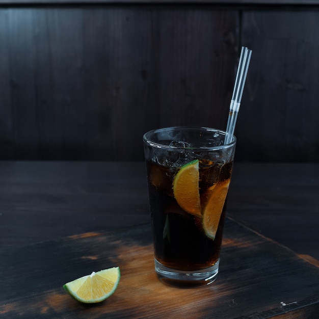 O delicioso coquetel original com adição de gelo, whisky e Coca-Cola, rodelas de limão sobre uma mesa de madeira de um restaurante. A apresentação original das bebidas alcoólicas no bar.