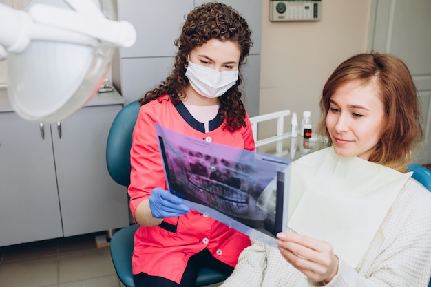 O dentista da casa da família mostra um raio-x. uma jovem sentada em uma recepção perto de um dentista. Dentista menina