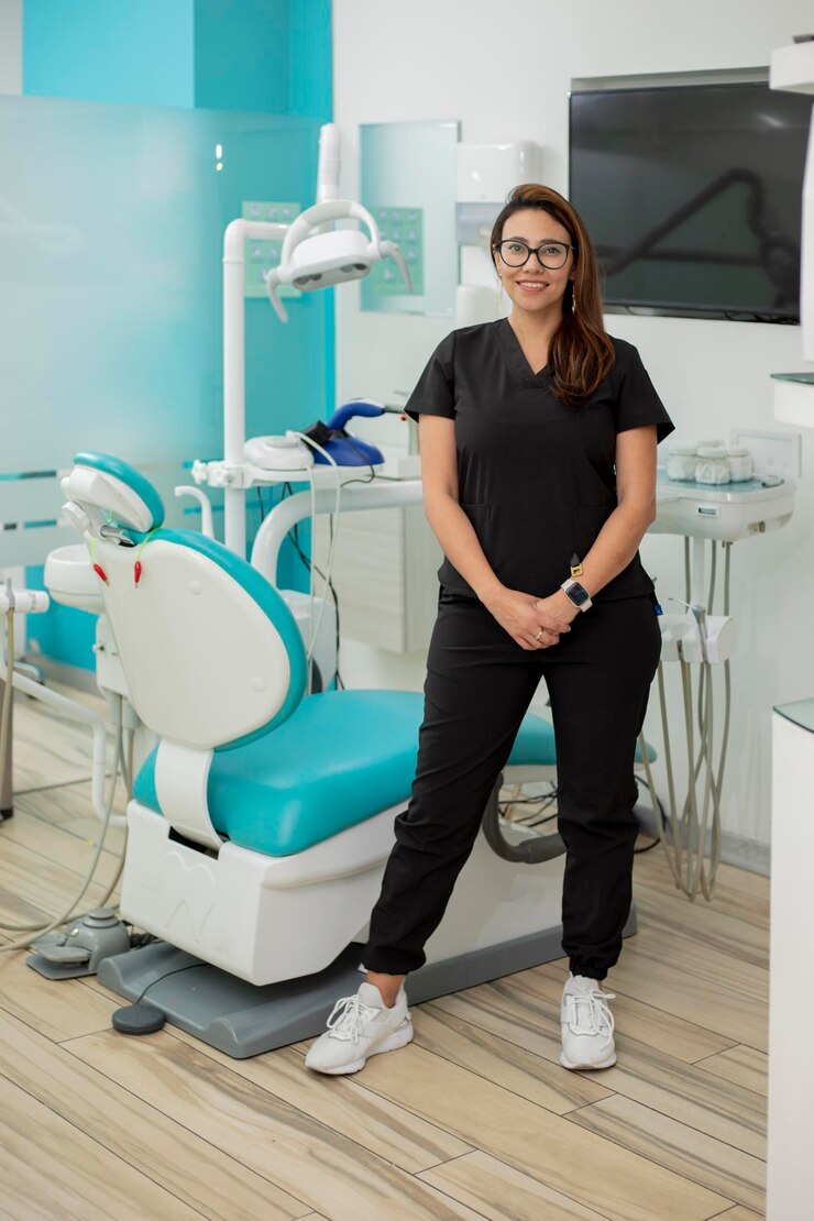O dentista de pé sorrindo e olhando para a câmera em seu consultório médico
