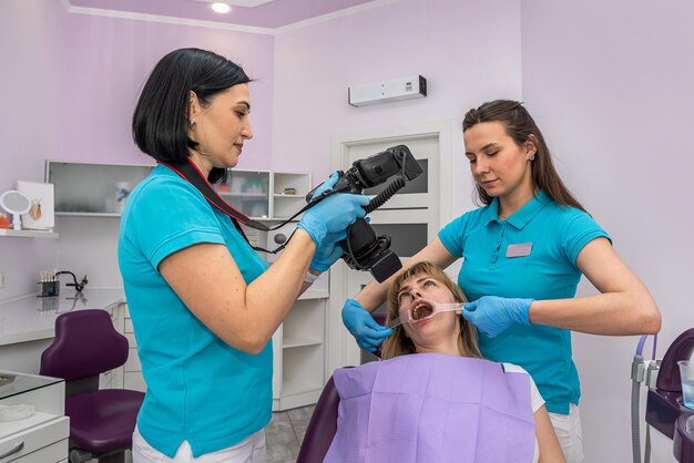 O dentista e seu assistente tiram fotos dos dentes do paciente na cadeira odontológica