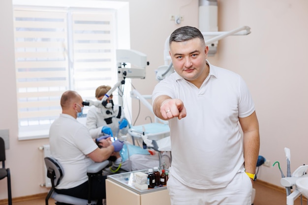 O dentista está em seu consultório odontológico Um dentista de uniforme branco trata os dentes de um paciente com um microscópio odontológico Consultório odontológico