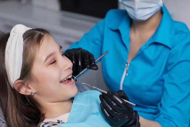 O dentista examina os dentes de leite da menina o tratamento dos dentes de leite o dentista segura um espelho nas mãos cárie em uma criança