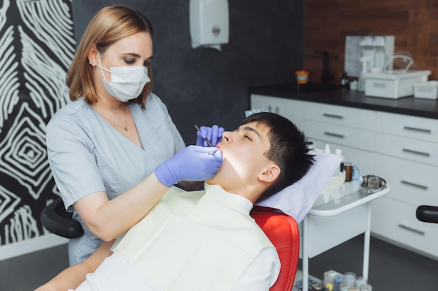 O dentista examina os dentes de um menino de 13 anos na clínica odontopediatria