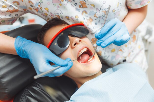 O dentista examina os dentes de um menino de 13 anos na clínica odontopediatria
