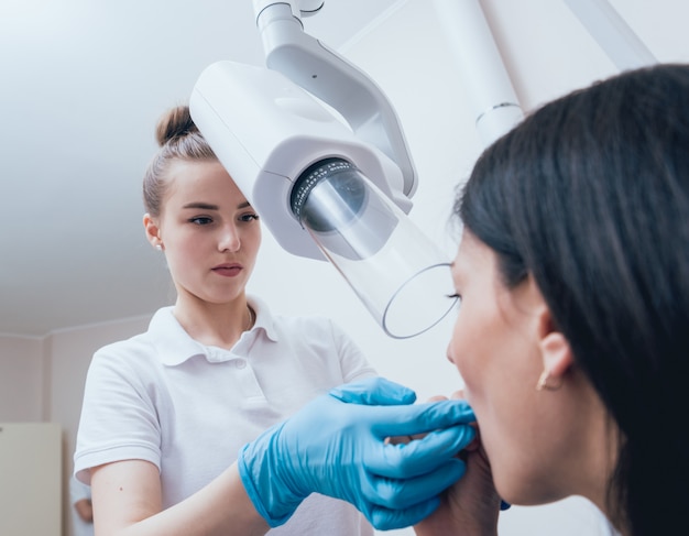 O dentista faz a imagem do raio X para a jovem mulher na clínica dental. Visando radiografia dentária.