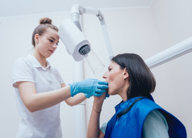 O dentista faz a imagem do raio X para a jovem mulher na clínica dental. Visando radiografia dentária.