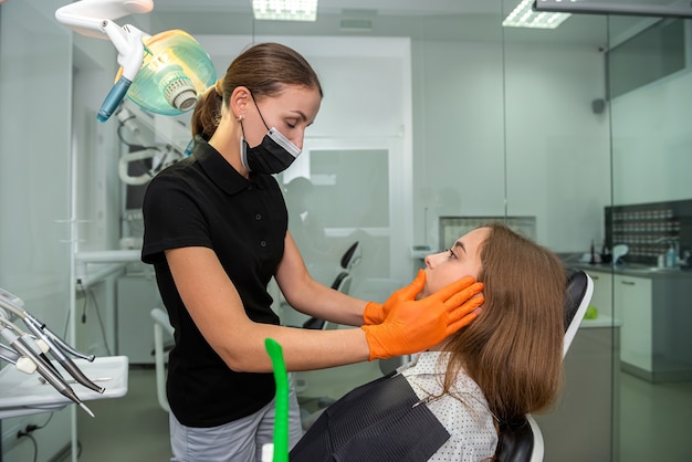 O dentista feminino realiza o exame inicial com as mãos tocando sua boca aberta. cuidados de saúde