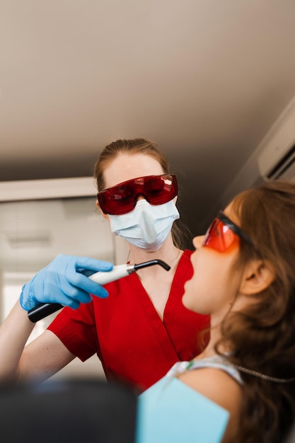 O dentista infantil trata e remove a cárie em um paciente Iluminação UV do procedimento de obturação do dente com fotopolímero Odontologia infantil