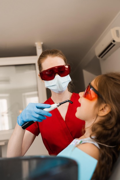 O dentista infantil trata e remove a cárie em um paciente Iluminação UV do procedimento de obturação do dente com fotopolímero Odontologia infantil