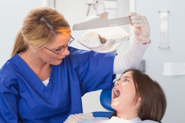 O dentista pediatra examina com a luz o paciente jovem