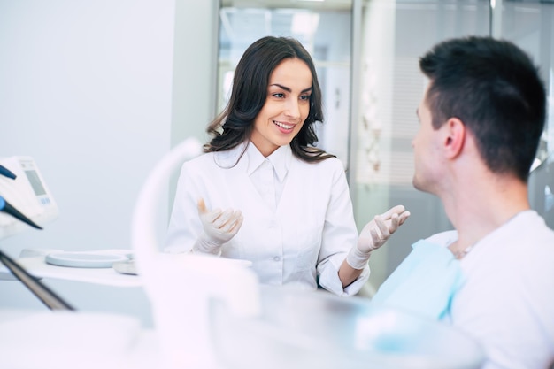 O dentista profissional na espaçosa sala do dentista está vestindo roupas médicas e dando algumas recomendações ao paciente após a consulta.