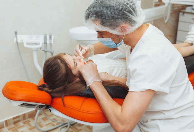 O dentista realiza um procedimento de exame em uma menina bonitinha menina sentada no consultório do dentista