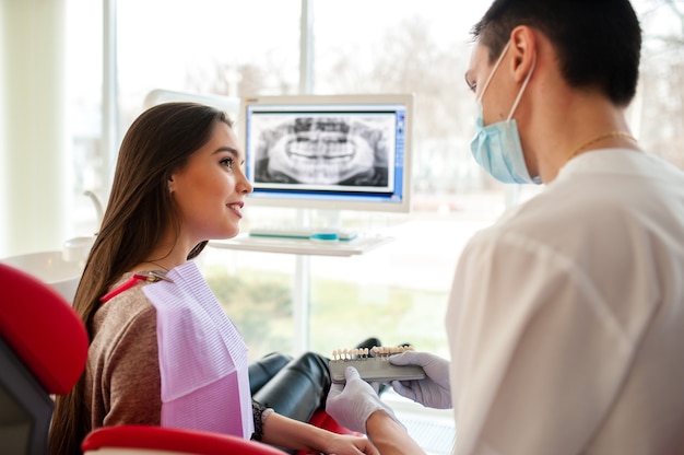 Foto o dentista seleciona a cor dos implantes dentários para uma linda garota.