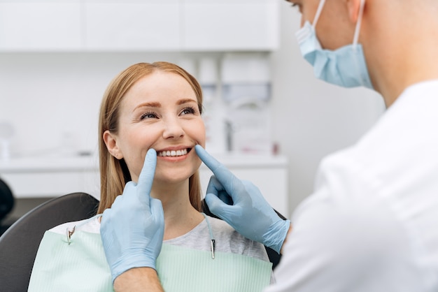 O dentista verifica os dentes de uma mulher atraente. O médico em luvas de borracha toca os dentes do paciente