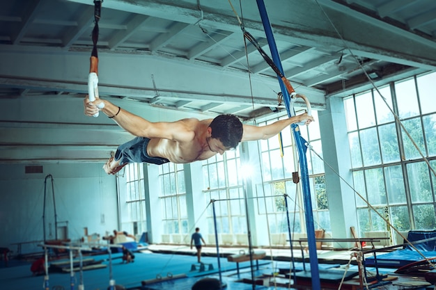 O desportista realizando difícil exercício de ginástica no ginásio. O esporte, exercício, ginasta, saúde, treinamento, conceito de atleta. Modelo de ajuste caucasiano