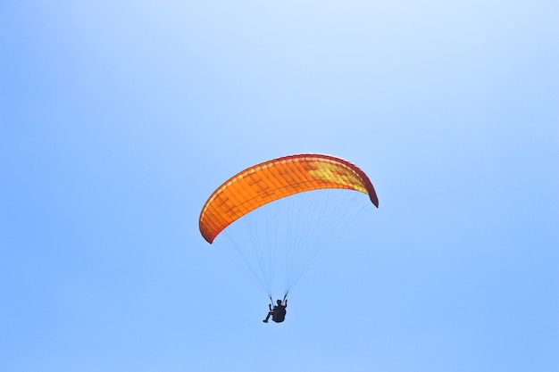 Foto o desportista voando em um parapente no céu azul