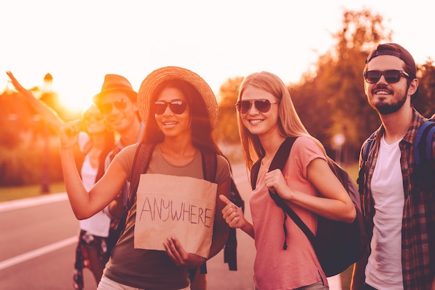 O destino está em qualquer lugar. Jovens lindos com mochilas pegando carona na estrada e parecendo felizes