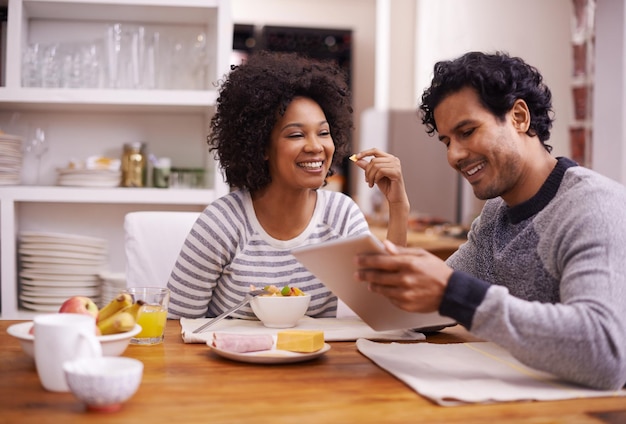 O dia é melhor quando começamos juntos Foto de um casal feliz tomando café da manhã juntos enquanto procura um tablet digital