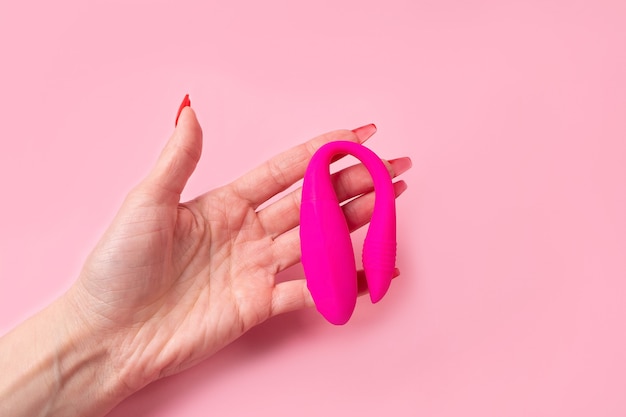 O Dildo na mão em um fundo rosa, brinquedo sexual