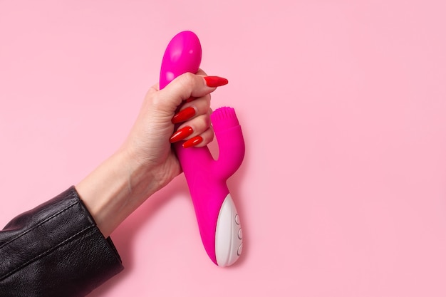 O dildo na mão em um fundo rosa, brinquedo sexual