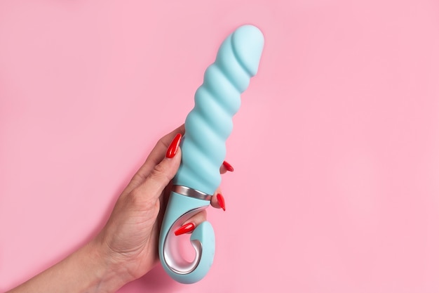 Foto o dildo na mão em uma parede rosa, brinquedo sexual