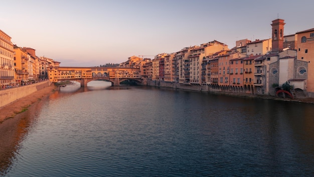 O dique do rio Arno com a ponte Ponte Vecchio e os edifícios da cidade velha ao pôr-do-sol em Florença, Itália