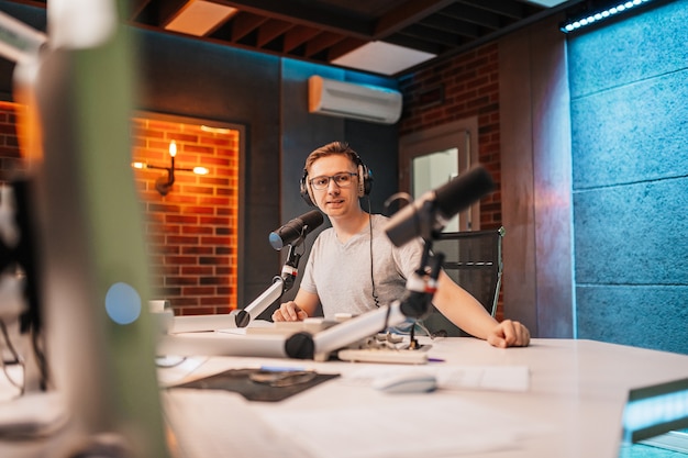 O DJ apresenta o programa e se comunica com o público que vai ao ar na estação de rádio. O locutor lê as notícias. Um locutor de rádio fala em um microfone e grava um podcast