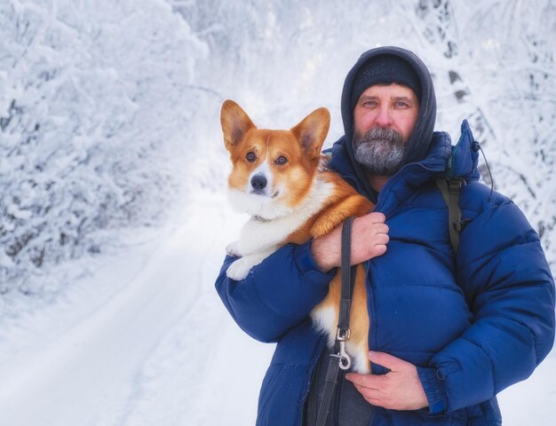 Foto o dono aquece seu cão congelado sob uma jaqueta quente em fortes geadas de inverno em uma caminhada na floresta