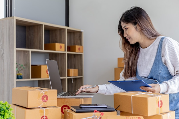 O dono da loja online está verificando o valor da compra no laptop e preparando a entrega, pacote para embalagem da mercadoria. venda online e conceitos de compras online.