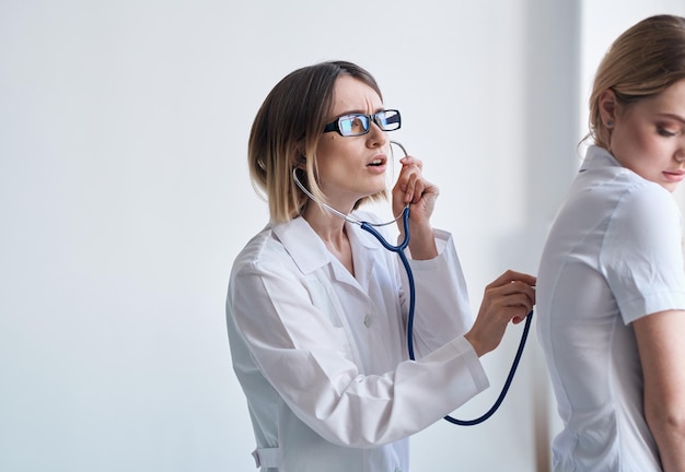 O doutor em um vestido médico com um estetoscópio examina um paciente em um fundo claro