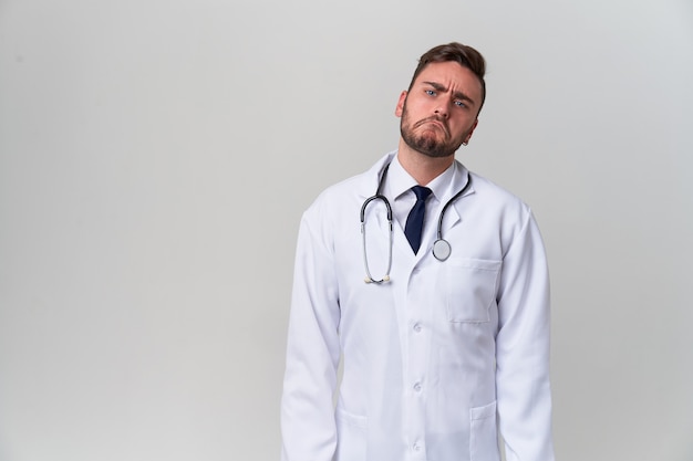 O doutor moderno considerável novo em um vestido médico branco está no estúdio em um branco. Estagiário de uma universidade médica.