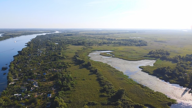 O drone sobrevoa um rio ondulante de cor azul cercado por uma vila local com vários edifícios e um Pantanal