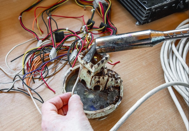 O eletricista cobre o fio de cobre com estanho usando um ferro de solda