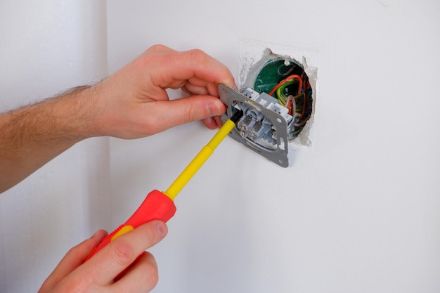 Foto o eletricista desenrosca o interruptor com uma chave de fenda em close-up nas mãos o trabalho de rotina de um eletricista verificação de contatos substituição do interruptor