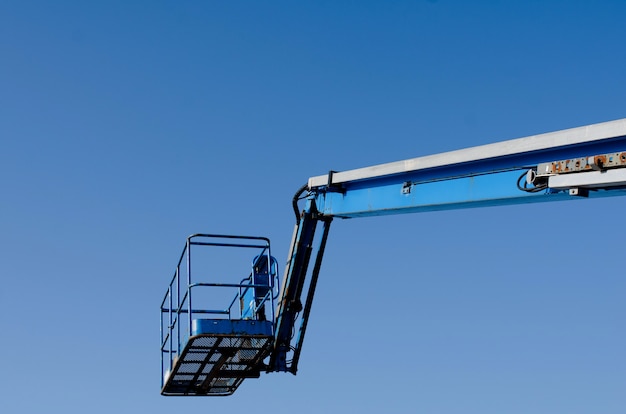 O elevador telescópico da lança ergueu-se no fundo do céu azul entregue no local da construção, pronto para ser usado por montadores de estruturas de aço, telhados e pintores