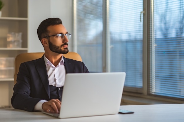 O empresário de óculos trabalhando com um laptop na mesa