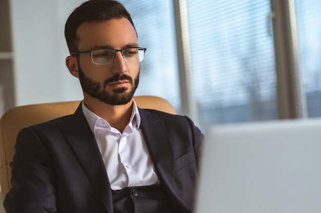 O empresário de óculos trabalhando com um laptop