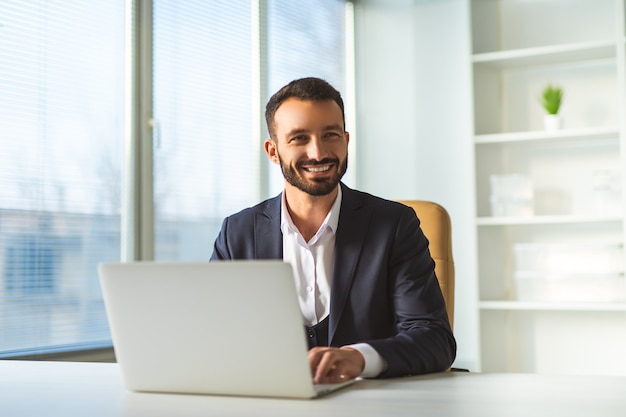 Foto o empresário feliz sentado à mesa com um laptop