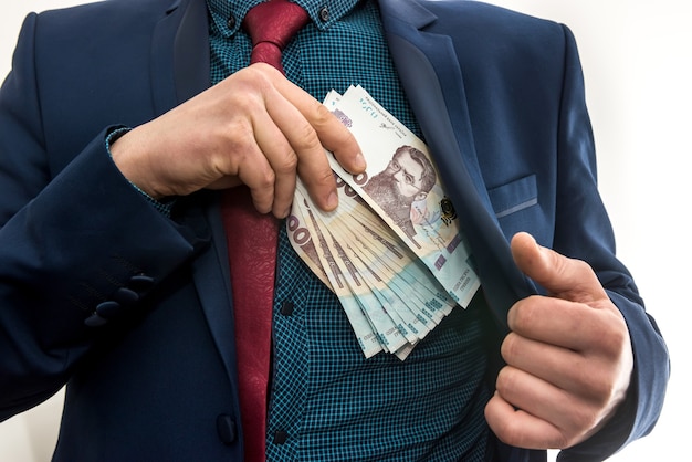 O empresário pega um maço de dinheiro ucraniano como suborno e se esconde dentro de uma jaqueta. Corrupção e um truque. UAH. 1000 novas notas